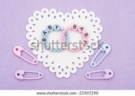 Baby bracelets and safety pins sitting on a white heart on purple background, baby bracelets