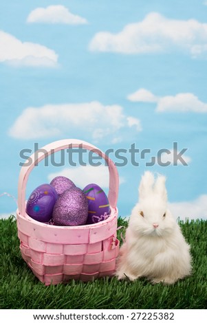 Wicker basket filled with Easter eggs and rabbit on green grass background, Easter basket