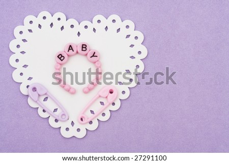 Baby bracelets and safety pins sitting on a white  heart on purple background, baby bracelets