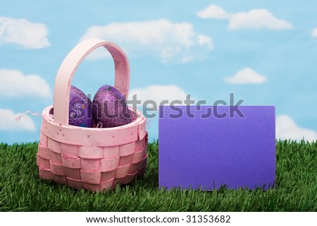 Wicker basket filled with Easter eggs and blank card on green grass background, Easter basket