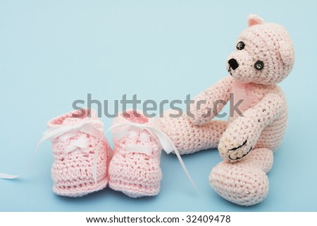 A pink handmade teddy bear and baby booties on a blue background, pink teddy bear