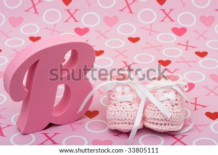 A pair of pink baby booties and the letter B on a pink love background, pink baby booties