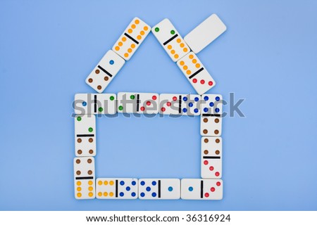 A house made of dominoes sitting on a blue background, falling housing market
