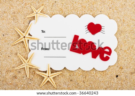 A white postcard with a red heart and the word love on a sand background, love postcard