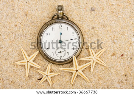 A pocket watch with starfish in the sand on the beach, summer vacation