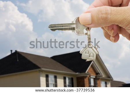 A key on a house keychain in a person?s hand on a house and sky background, unlocking your door