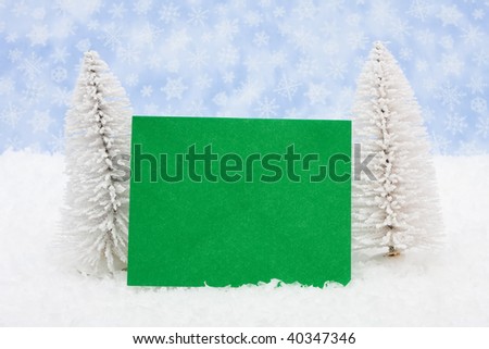 White evergreen trees sitting with a blank card with a blue snowflake background, blank card