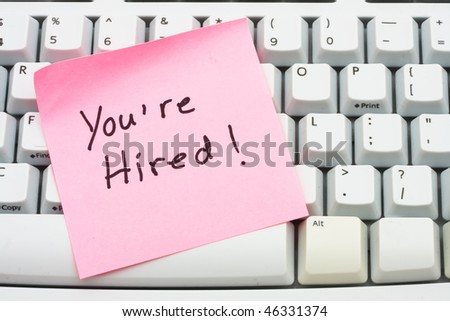 A pink sticky note saying your hired sitting on a computer keyboard, computer note