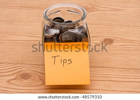 A jar full of change sitting on a wooden background, Tips are appreciated