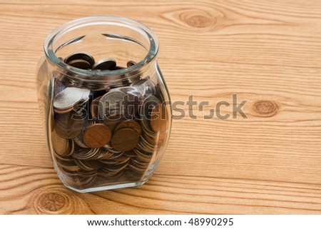 A jar full of change sitting on a wooden  background,  Saving money in your change jar