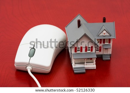 A model house sitting with a computer mouse on a red background, online real estate