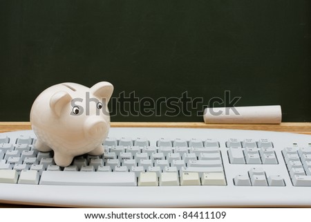 Computer keyboard on a desk with a piggy bank in front of a chalkboard with copy space, Cost of learning online