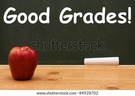 Apple on a desk in front of a chalkboard with text of Good Grades, Good Grades