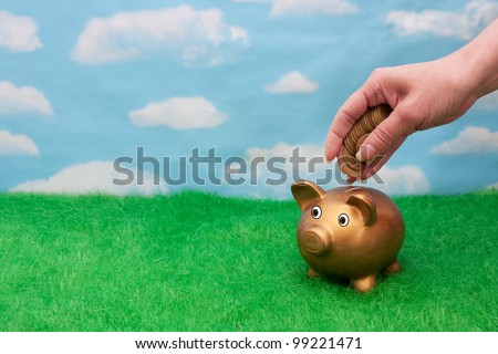 A gold piggy bank on grass with sky background with a hand and bunch gold coin, Adding a lot to you savings account