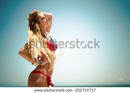 Sexy young blondie woman with large breasts and her hair blowing in the wind posing in a red bikini