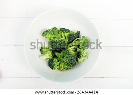 Broccoli in a white bowl isolated on a white wooden background