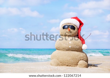 Smiling sandy snowman in red santa hat on the sea beach. Holiday concept can be used for New Year and Christmas Cards