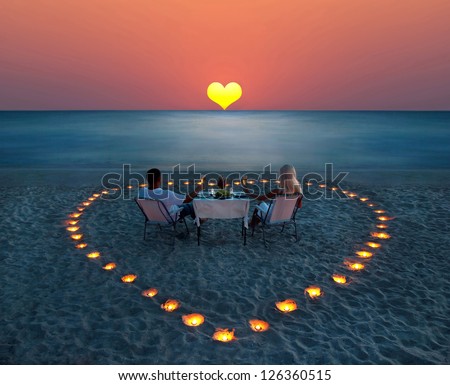 A young couple share a romantic dinner with candles heart on the sea sand beach A young couple share a romantic dinner with candles heart on the sea sand beach