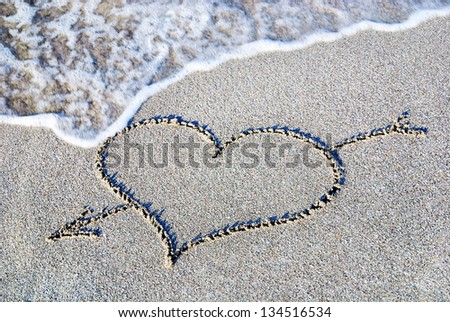 heart outline with arrow on the wet brilliance beach sand against wave
