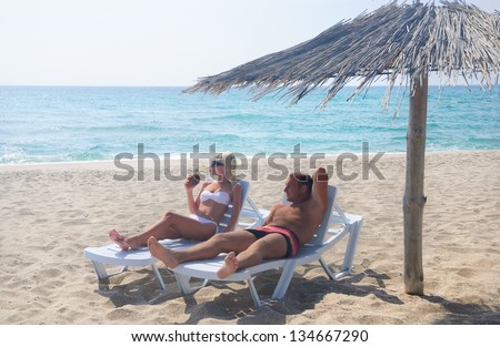 Young couple sunbathe in longue on the sea beach under sunshade