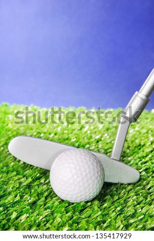 Golf ball and club on green field grass against blue sky - vertical image