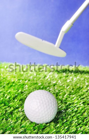 Golf ball and club on green field grass against blue sky - vertical image