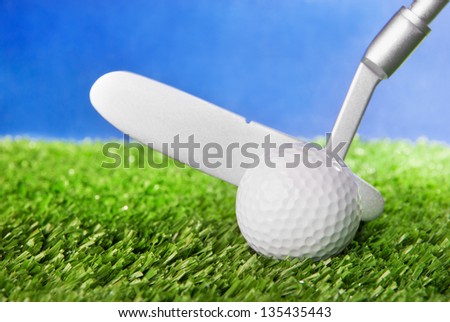 Golf ball and club on green field grass against blue sky - horizontal image