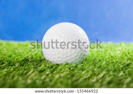 Golf ball on green field grass against blue sky - horizontal image
