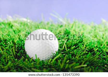 Golf ball on green field grass against blue sky - horizontal image