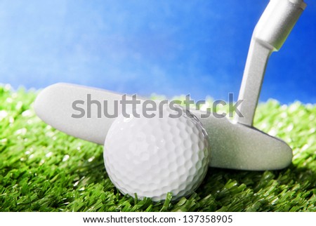 Golf ball and club on green field grass against blue sky - horizontal image