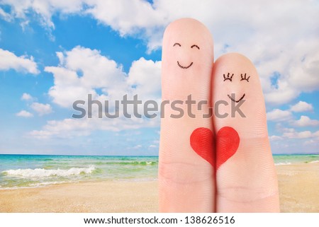 family vacation concept - a man and a woman hold on the red heart, painted at fingers against beautiful sea sand beach