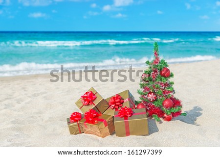 Christmas tree and golden gift with big red bow on the sea sandy beach Christmas vacation concept Christmas tree and golden gift with big red bow on the sea sandy beach Christmas vacation concept