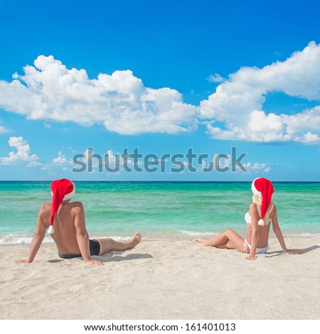 Lovers couple in red santa hats relaxing at tropical sandy beach - christmas vacation concept