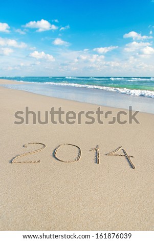 inscription 2014 on sea sand beach with the sun rays against wave foam and sky - vacation concept