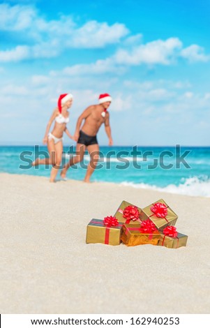 Running couple in santa hats at sea sand beach with christmas packed  golden gifts