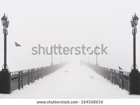 Bridge city landscape in foggy snowy winter day - walking couple, lanterns and doves flock - Ukraine, Donetsk