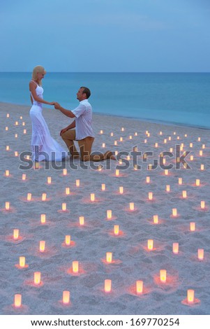 A man propose marriage to woman at sea beach in many candle lights against sunset- St.Valentines Day romantic concept