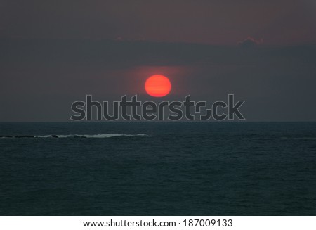 Bright sunset with large red sun under the ocean surface and wave foam