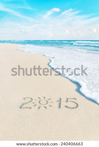 Year number on sea beach sand with the sun rays against wave edge and sky - vacation season 2015 concept
