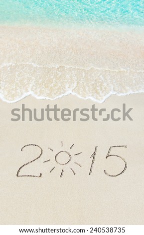 inscription 2015 on sea sand beach with the sun rays against wave foam and sky - vacation concept