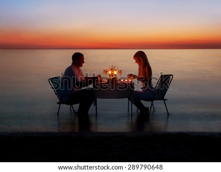 Loving couple share a romantic dinner with candles at sea beach in water against wonderful sunset