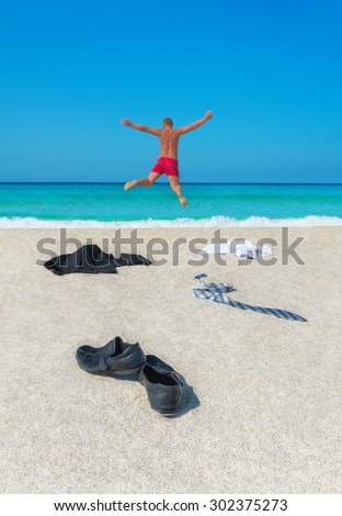 Happy man kicked off his office shoes, suit, tie to sand and jumping to sea waves -  long-awaited vacation or remote business success concept
