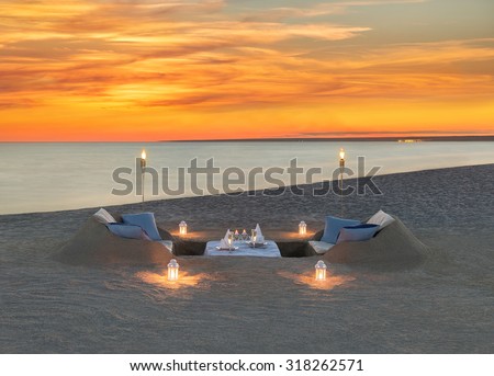 Romantic dinner with wine, candles, torches at sea beach during wonderful sunset. Honeymoon, proposal or wedding background concept.