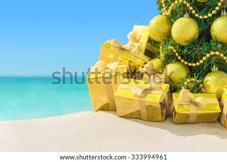 Christmas tree with golden decorations and packed gift boxes close-up at tropical sandy ocean beach. New Years vacation in hot countries background concept