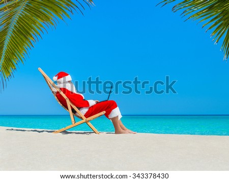 Santa Claus profile at tropical palm beach in wooden deckchair work using black laptop computer - Christmas  and New Year orders for gifts from children holiday concept