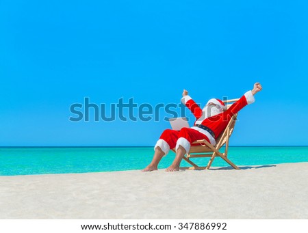 Santa Claus on deck chair hands up enjoy work using laptop computer at ocean sandy tropical beach - Christmas  and New Year vacation and travel destinations in hot countries concept