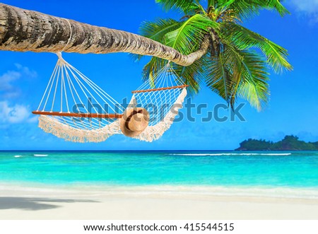 Romantic cozy hammock with straw hat in the shadow of coconut palm tree at tropical paradise ocean beach in bright sunny summer day - vacation background