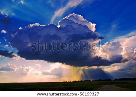 Big cumuli cloud with sun rays and rain against blue sky