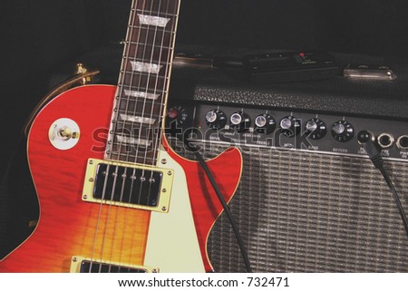 Classic electric guitar with sunburst pattern leaning against an amplifier. Electronic tuner on top of amp.