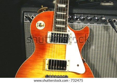 Classic sunburst pattern electric guitar leaning against an amplifier. View of both pickups. Electronic tuner on top of amp.